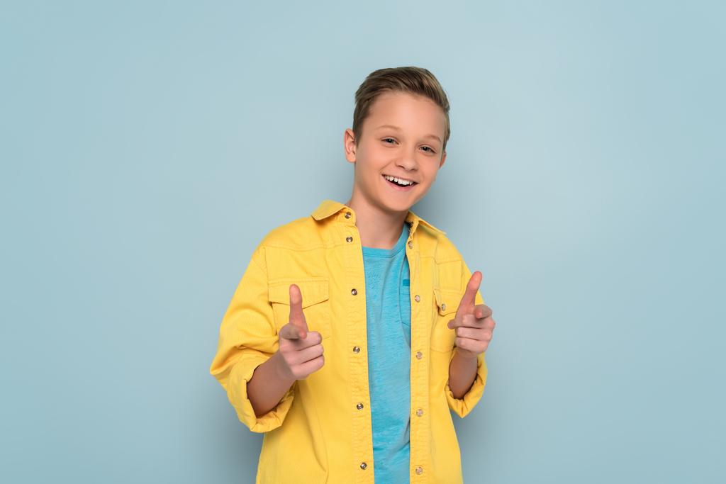 smiling and cute kid pointing with fingers on blue background  - Photo, Image