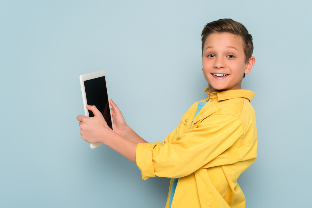 garoto sorrindo segurando tablet digital e olhando para a câmera no fundo azul
  - Foto, Imagem