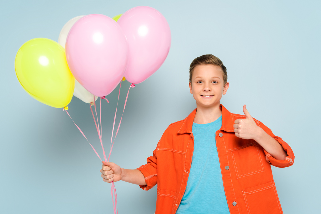 Elinde balonlarla gülümseyen ve mavi arka planda görünen bir çocuk.  - Fotoğraf, Görsel