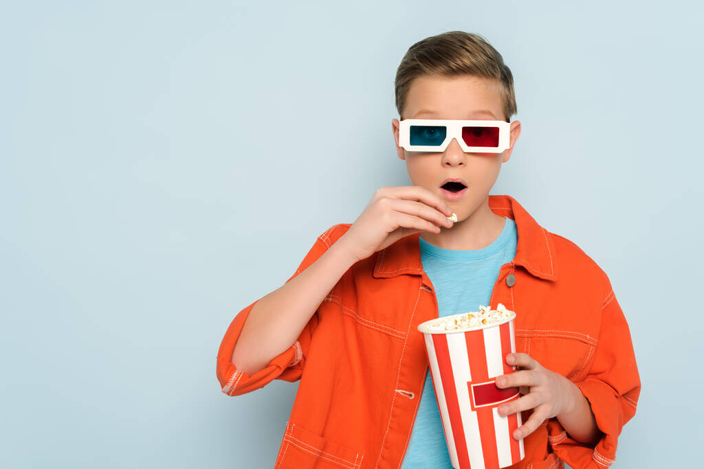 σοκαρισμένο παιδί με 3d ποτήρια τρώει ποπ κορν σε μπλε φόντο  - Φωτογραφία, εικόνα