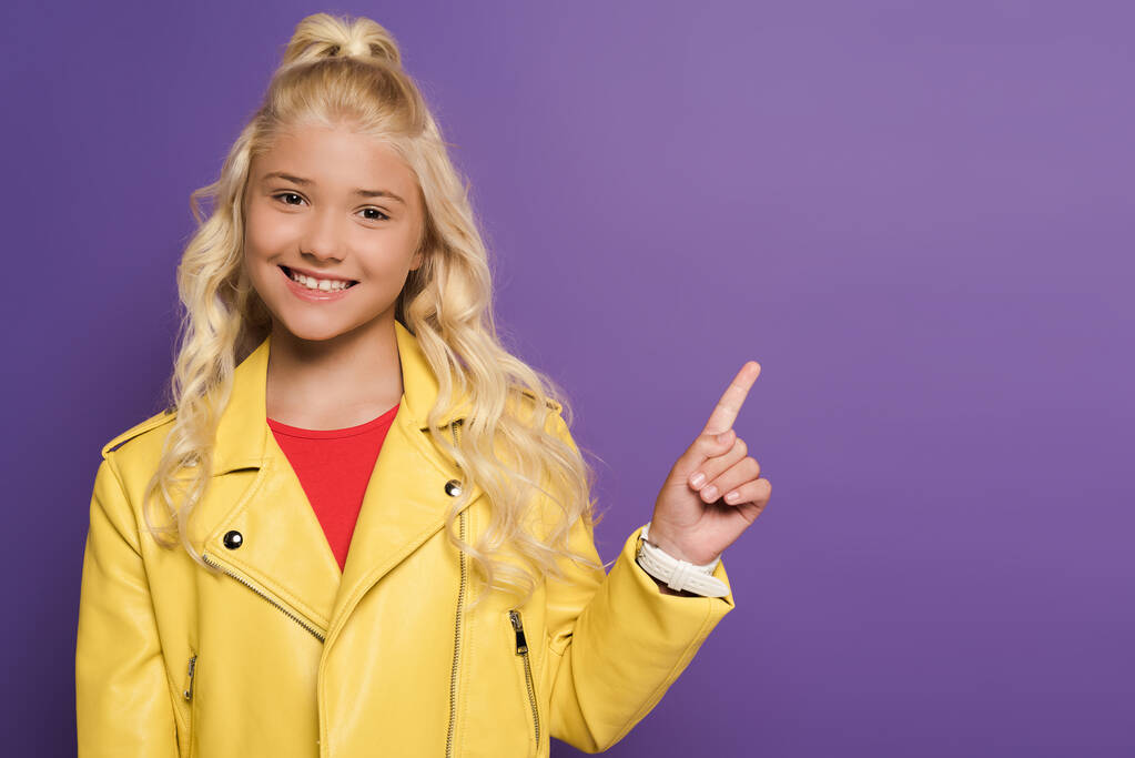 smiling and cute kid pointing with finger on purple background  - Photo, Image