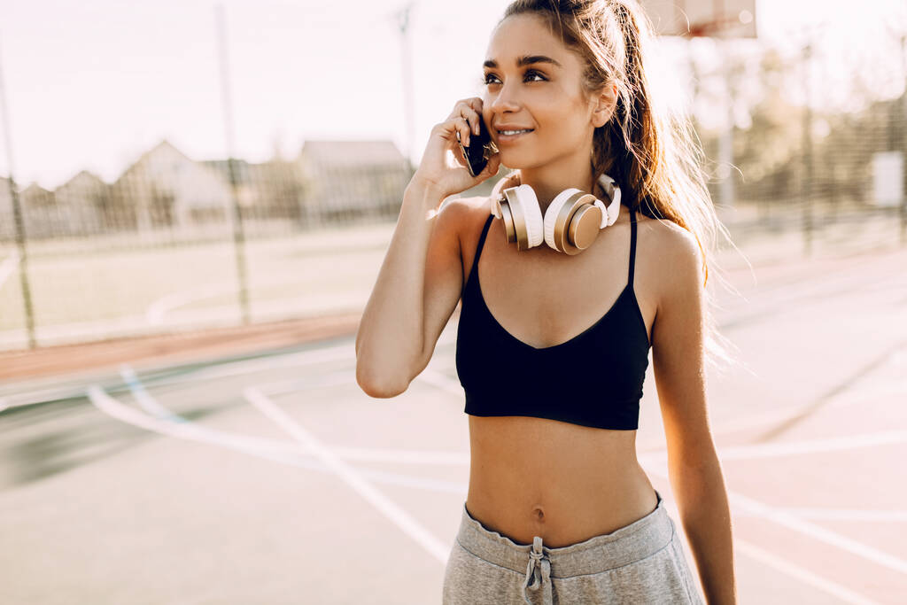 Obraz šťastné mladé atletické ženy venku, mluvení v mobilním telefonu, po cvičení - Fotografie, Obrázek
