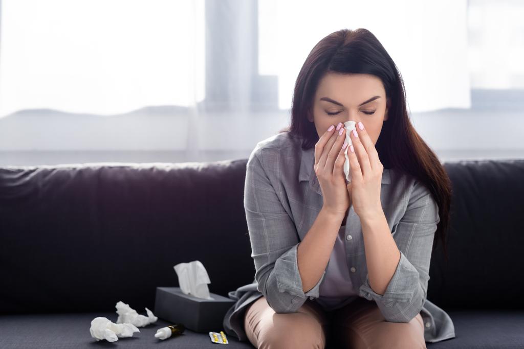mujer con alergia estornudando en servilleta mientras está sentada en el sofá
  - Foto, imagen