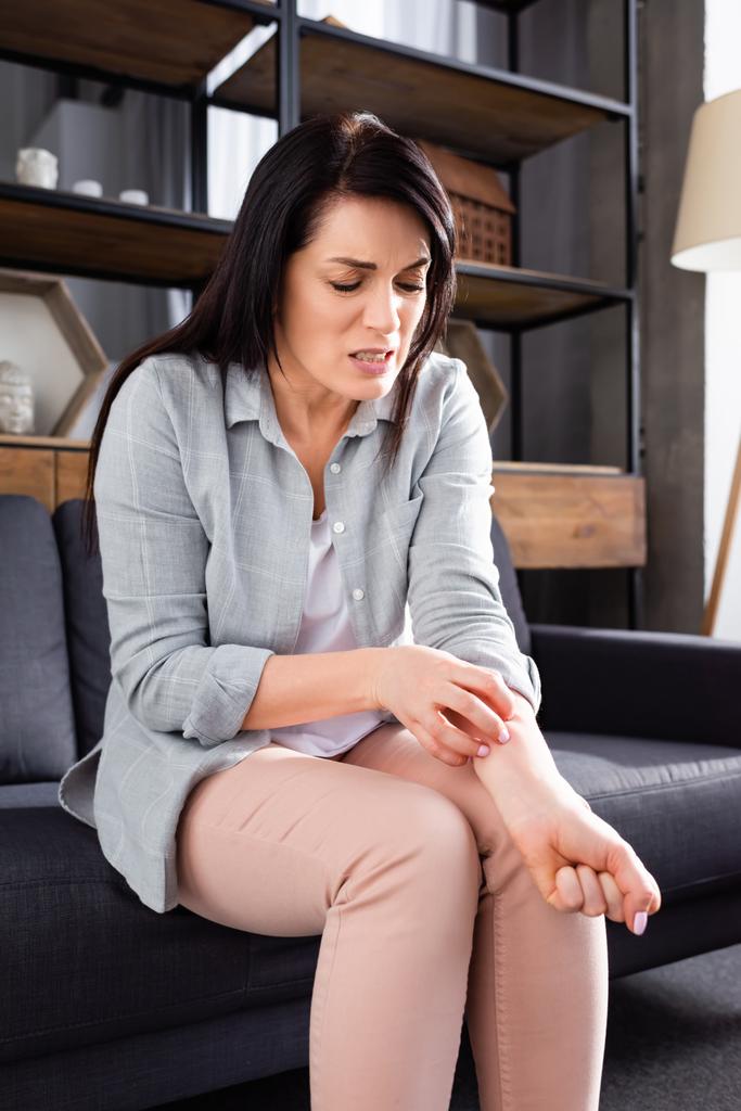 mujer alérgica rascarse la mano mientras está sentado en el sofá
  - Foto, imagen