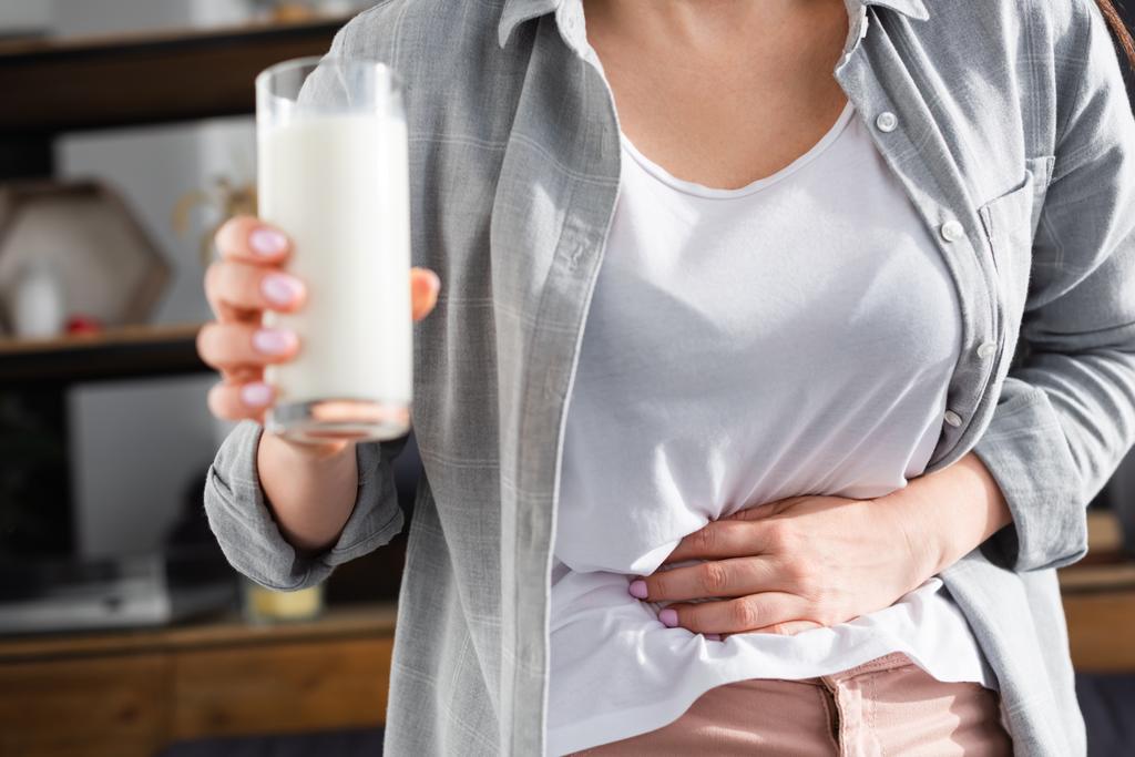 bijgesneden zicht op vrouw met lactose-intolerantie die een glas melk vasthoudt terwijl ze de maag aanraakt  - Foto, afbeelding