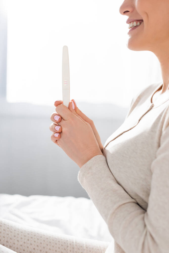 καλλιεργημένη άποψη του χαμογελαστού γυναίκα που κατέχουν τεστ εγκυμοσύνης  - Φωτογραφία, εικόνα
