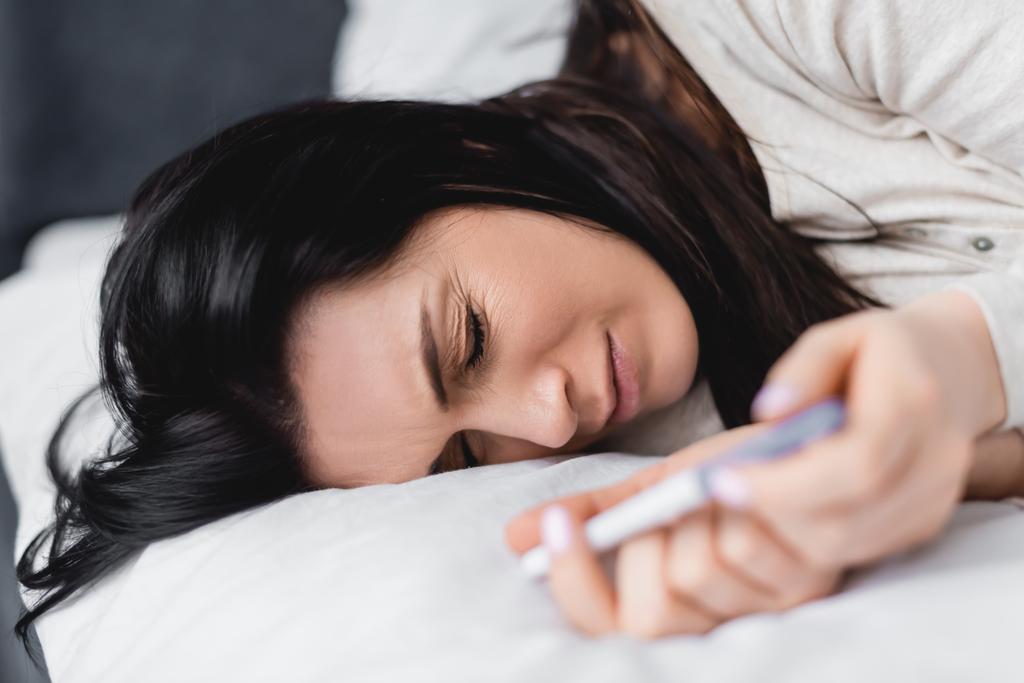 selectieve focus van de vrouw die op bed ligt en een zwangerschapstest uitvoert met negatief resultaat  - Foto, afbeelding