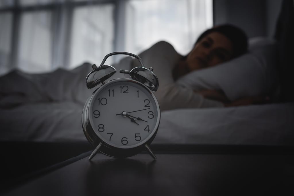 enfoque selectivo del reloj despertador en la mesita de noche cerca de la mujer despierta
  - Foto, imagen