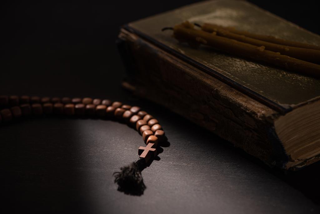 selective focus of holy bible with candles and rosary with cross in dark with sunlight - Photo, Image