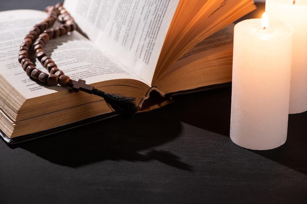 Sainte Bible avec chapelet sur fond noir foncé avec des bougies allumées
 - Photo, image