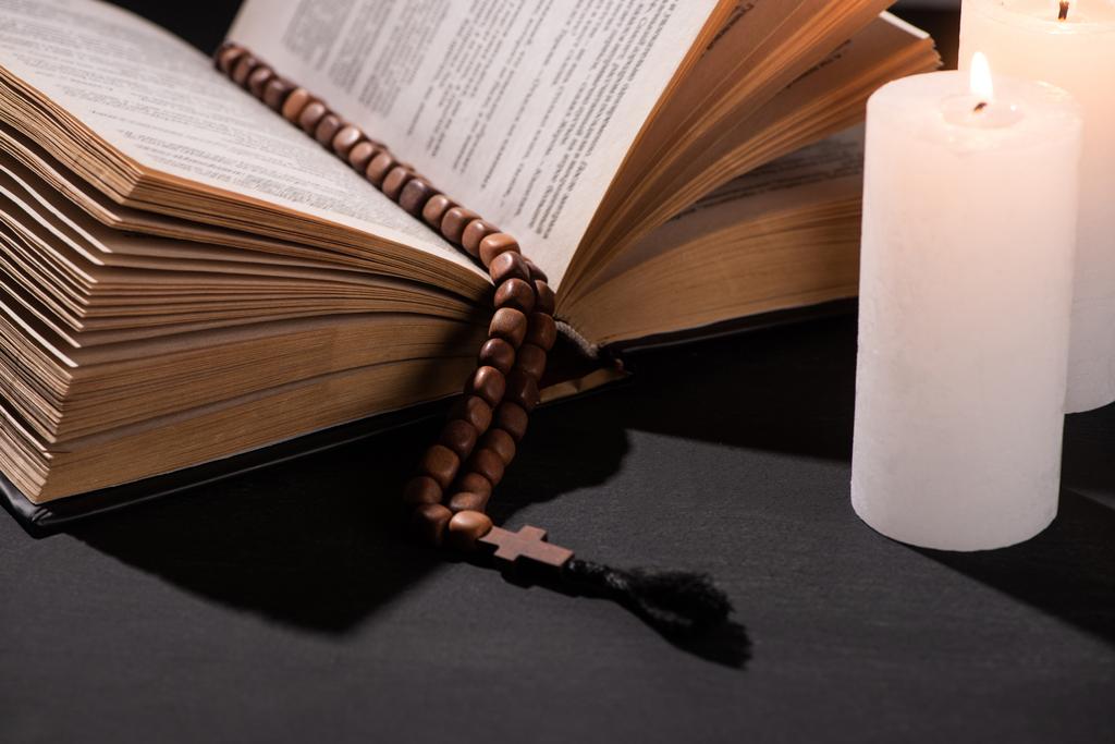 Bíblia sagrada com rosário no fundo escuro preto com velas acesas
 - Foto, Imagem
