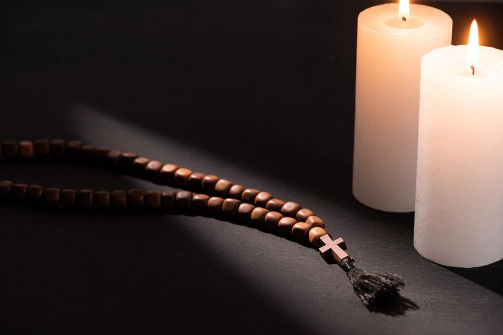 rosario sobre fondo negro oscuro con velas encendidas
 - Foto, Imagen
