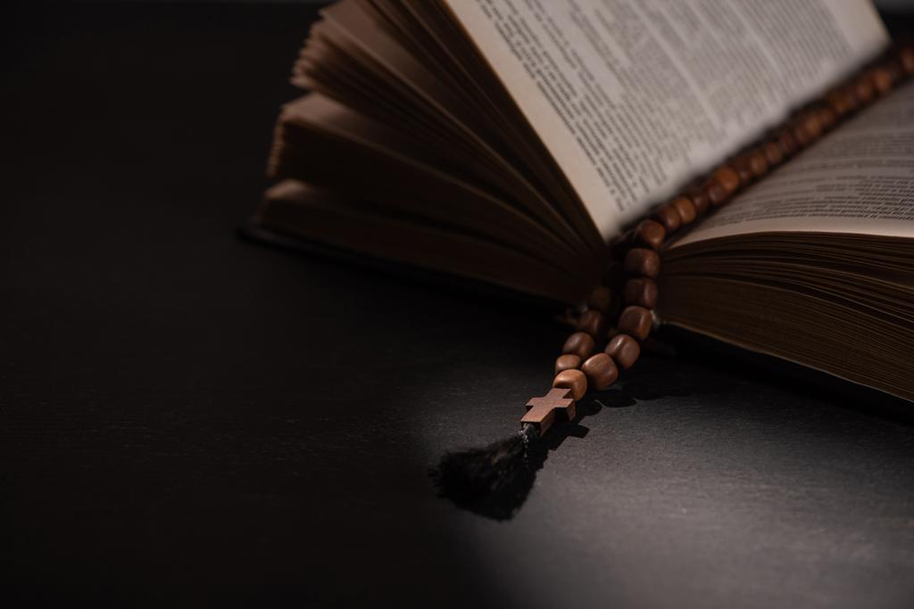 heilige bijbel met rozenkrans op zwarte donkere achtergrond met zonlicht  - Foto, afbeelding