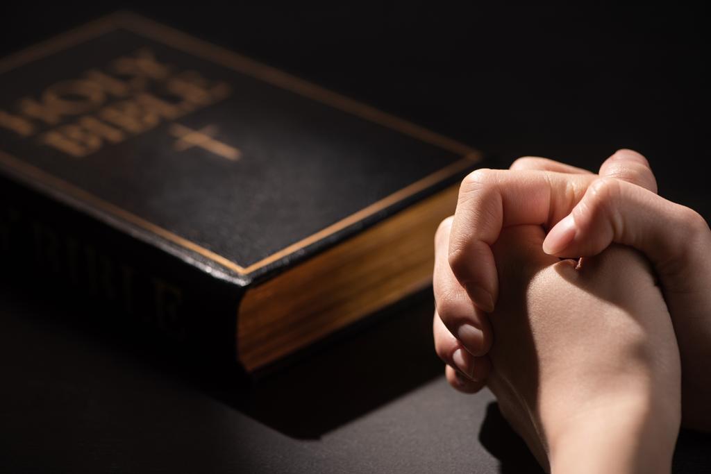 cropped view of woman praying near holy bible in dark - Photo, Image