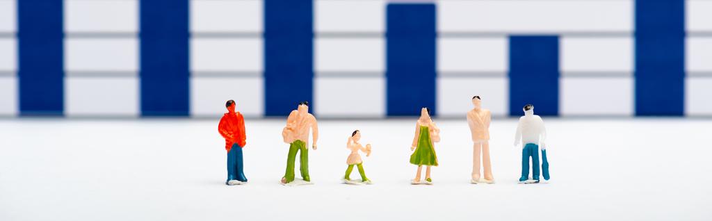 Panoramaaufnahme von Plastikfiguren auf weißer Oberfläche mit blauen Diagrammen im Hintergrund, Konzept der Gleichberechtigung - Foto, Bild
