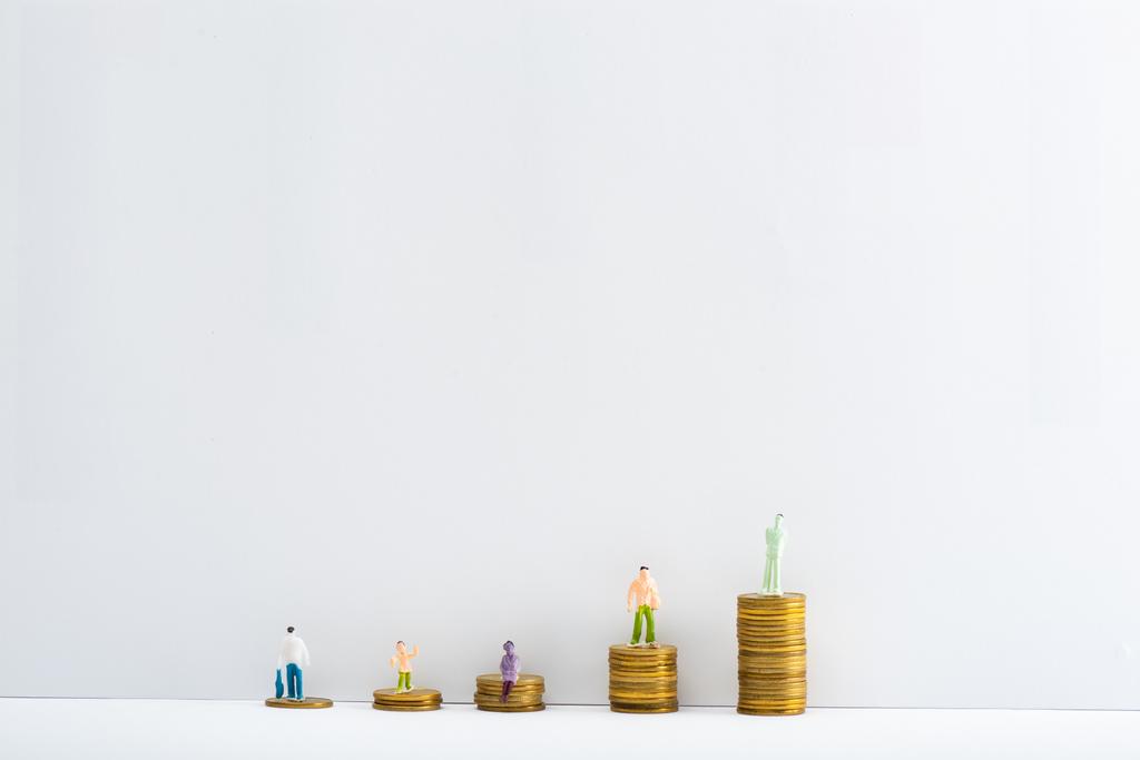 Plastic people figures on stacked coins on white surface on grey background, concept of financial equality - Photo, Image
