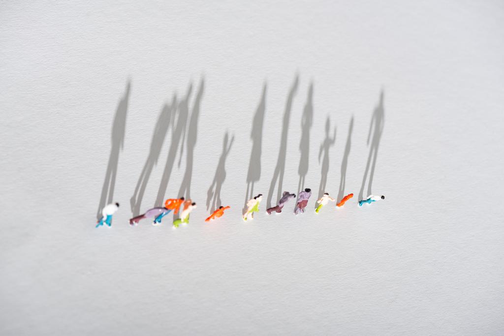 Vista dall'alto di fila di figure di persone di plastica su superficie bianca con ombra
 - Foto, immagini