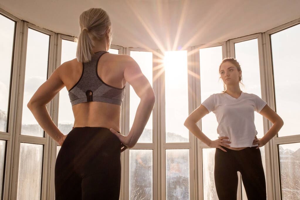 Dwie piękne dziewczyny ćwiczące razem ze słońcem świecącym przez okno. Fitness, styl życia jogi - Zdjęcie, obraz