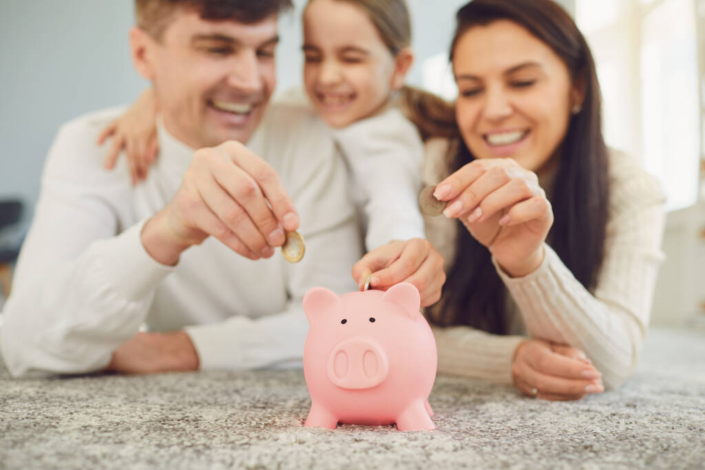 Ευτυχισμένη οικογένεια εξοικονομεί χρήματα σε ένα γουρουνάκι τράπεζα χοίρων. - Φωτογραφία, εικόνα