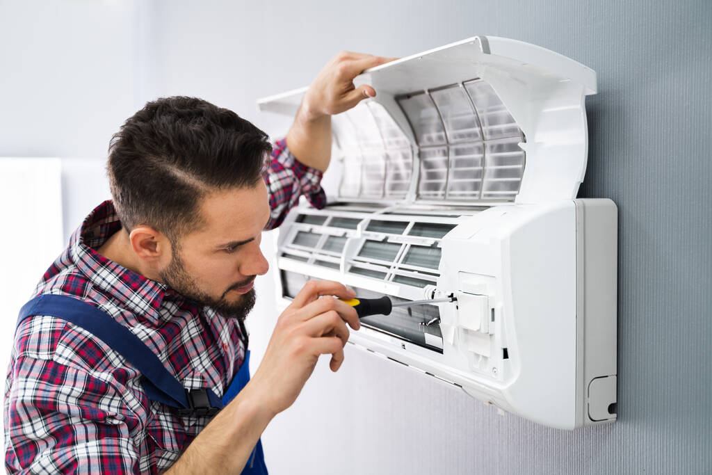 Glücklicher männlicher Techniker repariert Klimaanlage mit Schraubenzieher - Foto, Bild