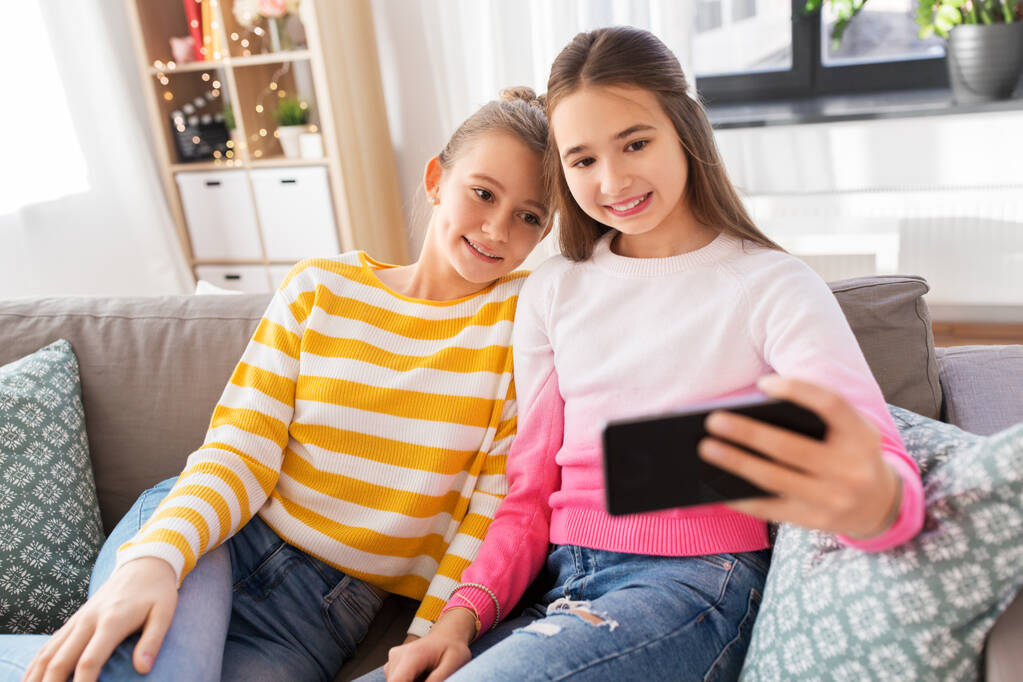 Mutlu kızlar evde akıllı telefonlarıyla selfie çekiyorlar. - Fotoğraf, Görsel