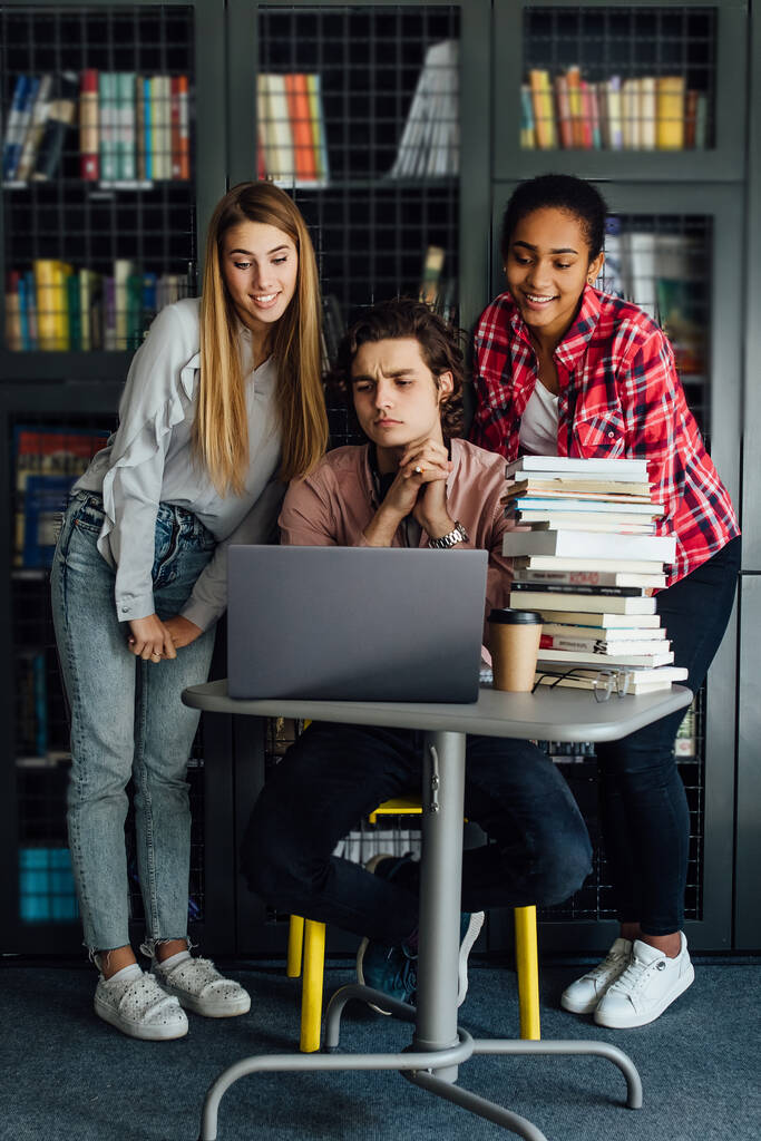 Portret van drie gelukkige jonge studenten die tijd doorbrengen in de bibliotheek terwijl ze zich voorbereiden op de les. - Foto, afbeelding