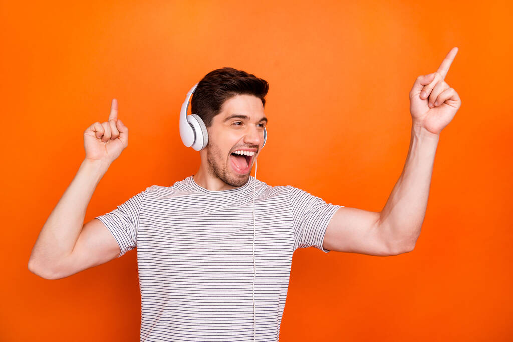 Photo of funky cool guy cheerful party mood chilling listening earphones direct fingers up empty space wear striped t-shirt isolated bright orange color background - Φωτογραφία, εικόνα