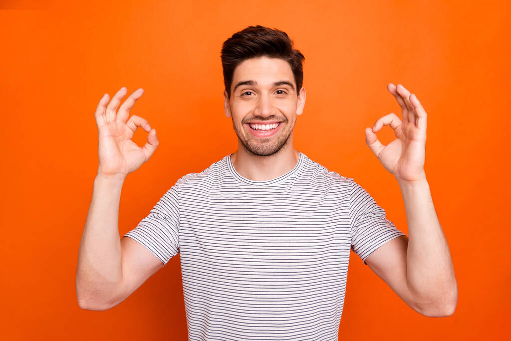 Photo of cool funny guy raise hands showing okey symbols cheerful person expressing agreement wear casual striped t-shirt isolated bright orange color background - Fotó, kép