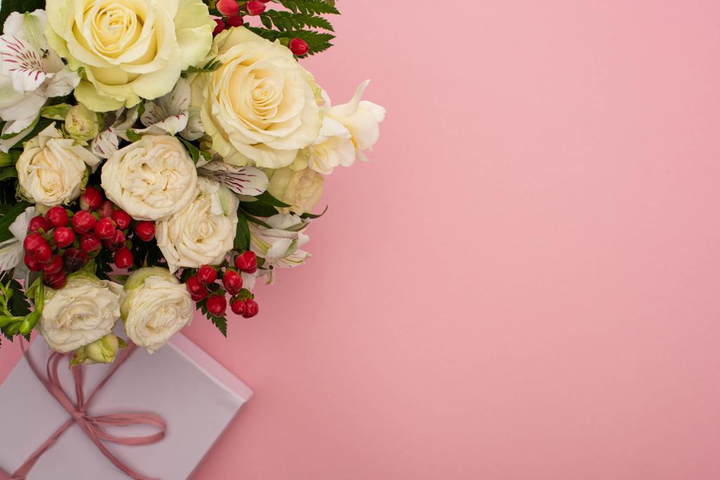 vrchní pohled na kytice květin ve slavnostní dárkové krabici s lukem na růžovém pozadí - Fotografie, Obrázek