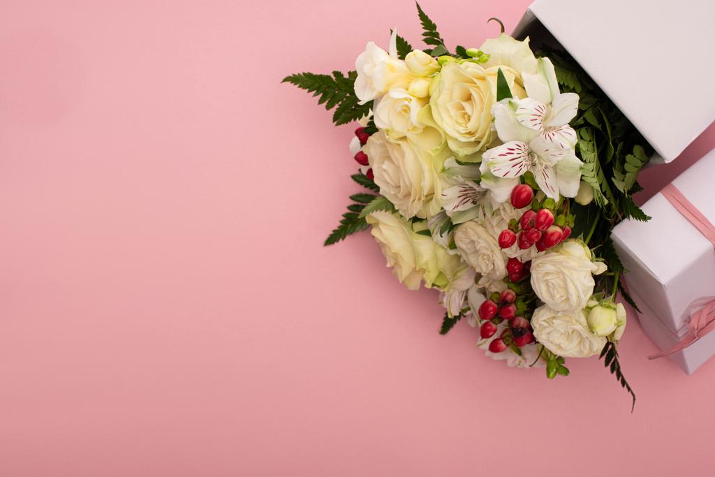 ピンクを背景に弓を持つお祝いのギフトボックスの花の花束のトップビュー - 写真・画像