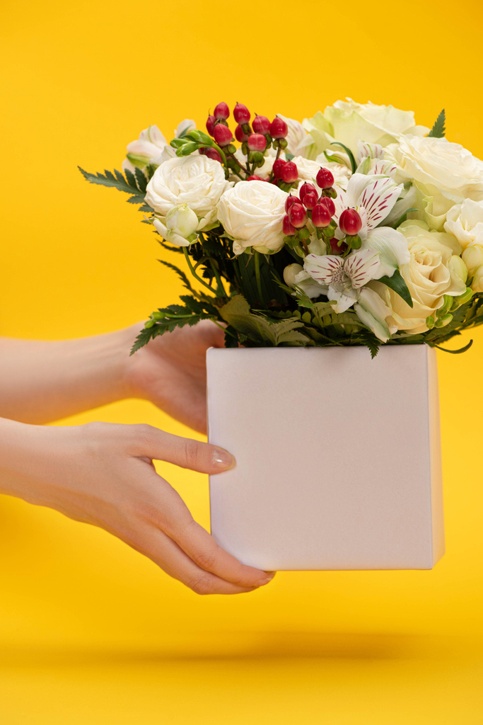 abgeschnittene Ansicht einer Frau mit frühlingshaftem Blumenstrauß im Kasten auf gelbem Hintergrund - Foto, Bild