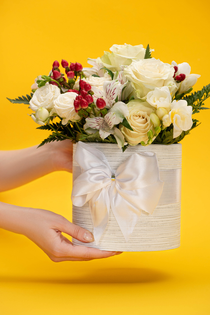 黄色の弓でお祝いのギフトボックスで花の春の新鮮な花束を保持する女性のクロップドビュー - 写真・画像