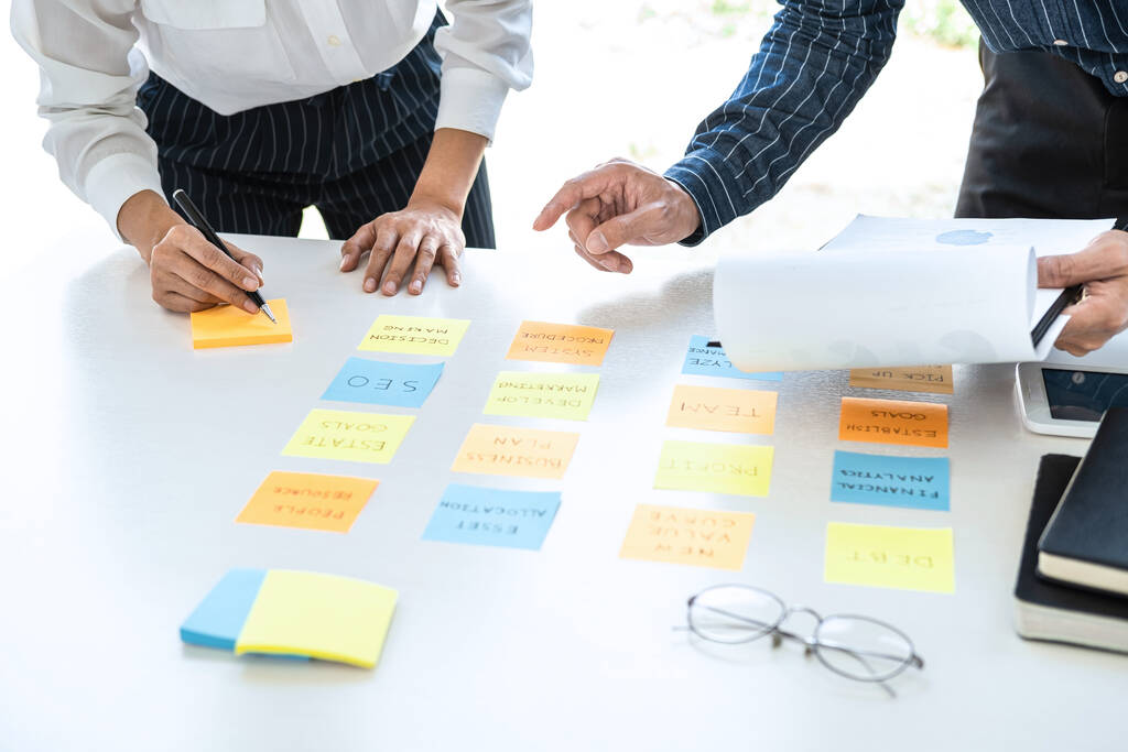 Two creative business people meeting and planning use post it notes sticky note on desk to share idea, Analysis data chart and graph with teamwork strategy brainstorming in office. - Photo, Image