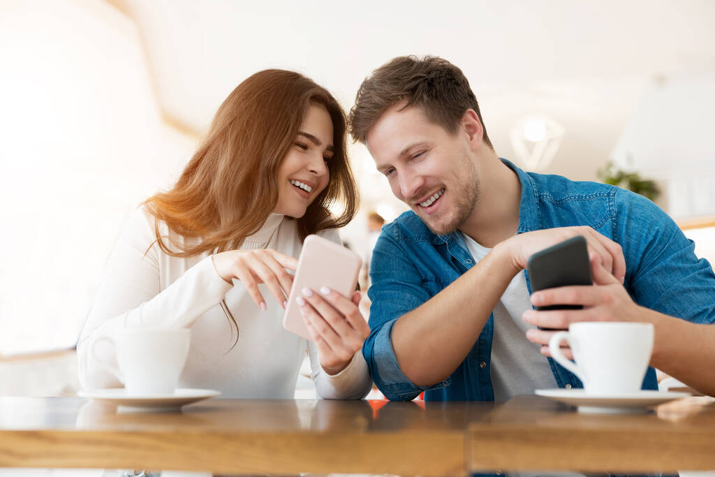 mladý pár krásná žena a pohledný muž sedí v kavárně během přestávky na kávu, oba drží smartphony, koncept vývoje technologií. - Fotografie, Obrázek
