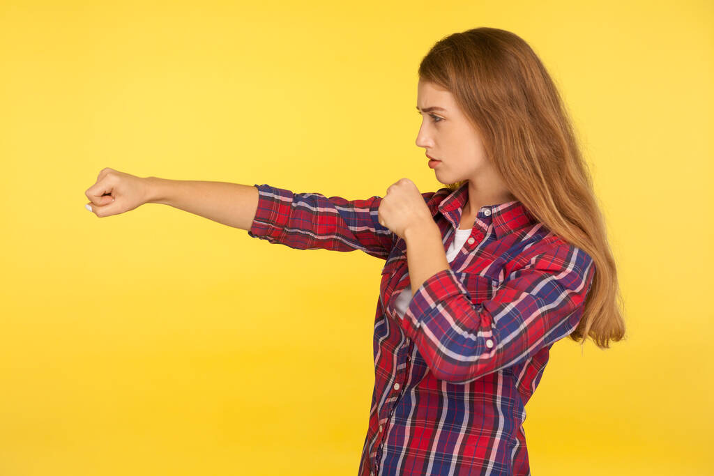 Профіль сильної і рішучої дівчини-імбиру в картатій сорочці, що пробиває повітря кулаком і виглядає впевнено, жіноча боротьба, бойовий дух. критий студійний знімок ізольований на жовтому фоні
 - Фото, зображення