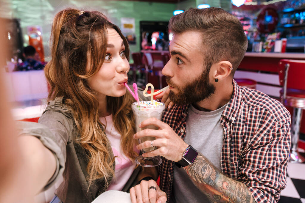 Obrázek legrační emocionální pozitivní mladý milující pár v retro světlé ulici potravin kavárna se selfie podle kamery pití koktejl. - Fotografie, Obrázek