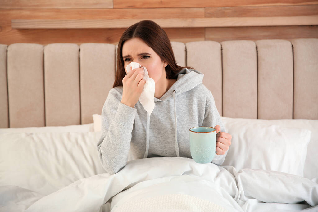 Nemocná mladá žena s šálkem horkého nápoje doma v posteli. Virus chřipky - Fotografie, Obrázek