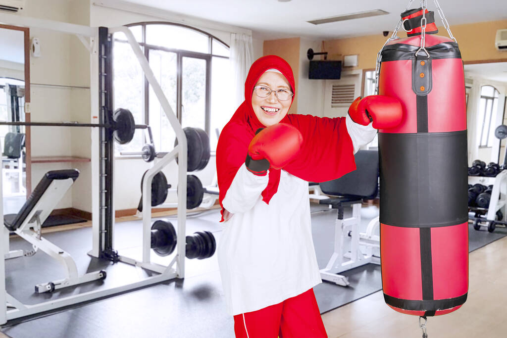 Porträt einer betagten Frau, die im Fitnessstudio mit Boxsäcken schlägt - Foto, Bild
