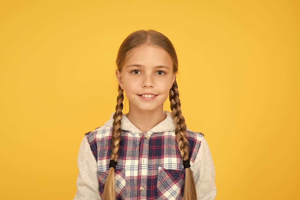 Słodka, pleciona dziewczyna. Długie włosy. Mała dziewczynka w kratkę. Szczęśliwego międzynarodowego dnia dla dzieci. Żółte tło małej dziewczynki. Dobry pomysł na nastrój. Pozytywne wibracje. Szczere emocje. Dobrze się bawię - Zdjęcie, obraz