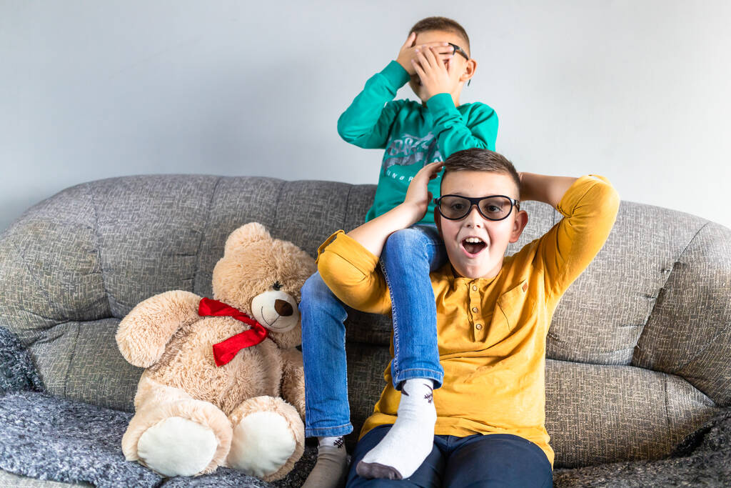 Chicos lindos, molesta ver una película de miedo con gafas 3d, sentado en el sofá en la sala de estar, junto con el juguete de oso de peluche - Foto, imagen