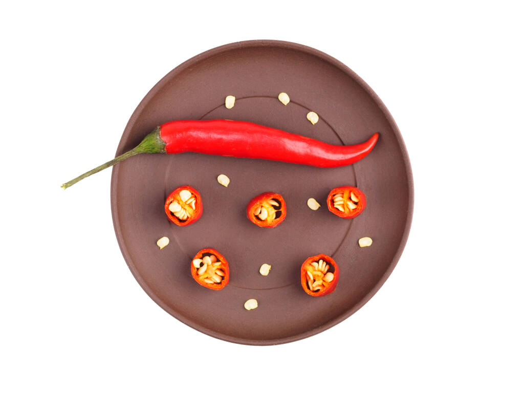 Red chili on brown clay plate isolated on white. Indian cuisine, ayurveda, naturopathy concept - 写真・画像