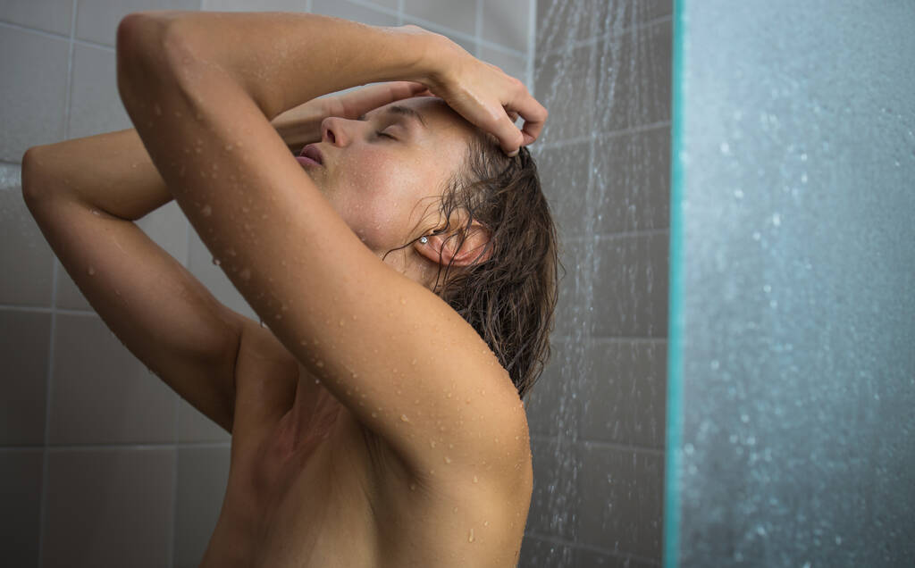 Красивая молодая женщина, принимающая долгий горячий душ, моет волосы в современной ванной комнате - Фото, изображение