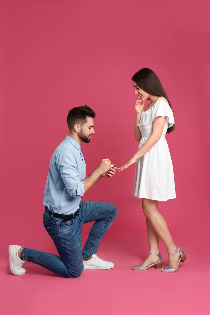Mann mit Verlobungsring macht Freundin Heiratsantrag vor purpurrotem Hintergrund - Foto, Bild
