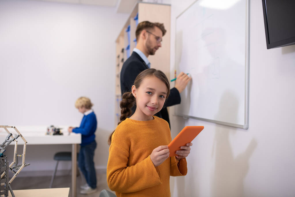 man leraar schrijven op whiteboard, meisje holding tablet, jongen staan aan bureau - Foto, afbeelding