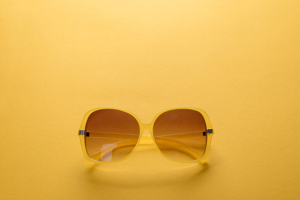 Folded sunglasses on yellow background - Photo, Image