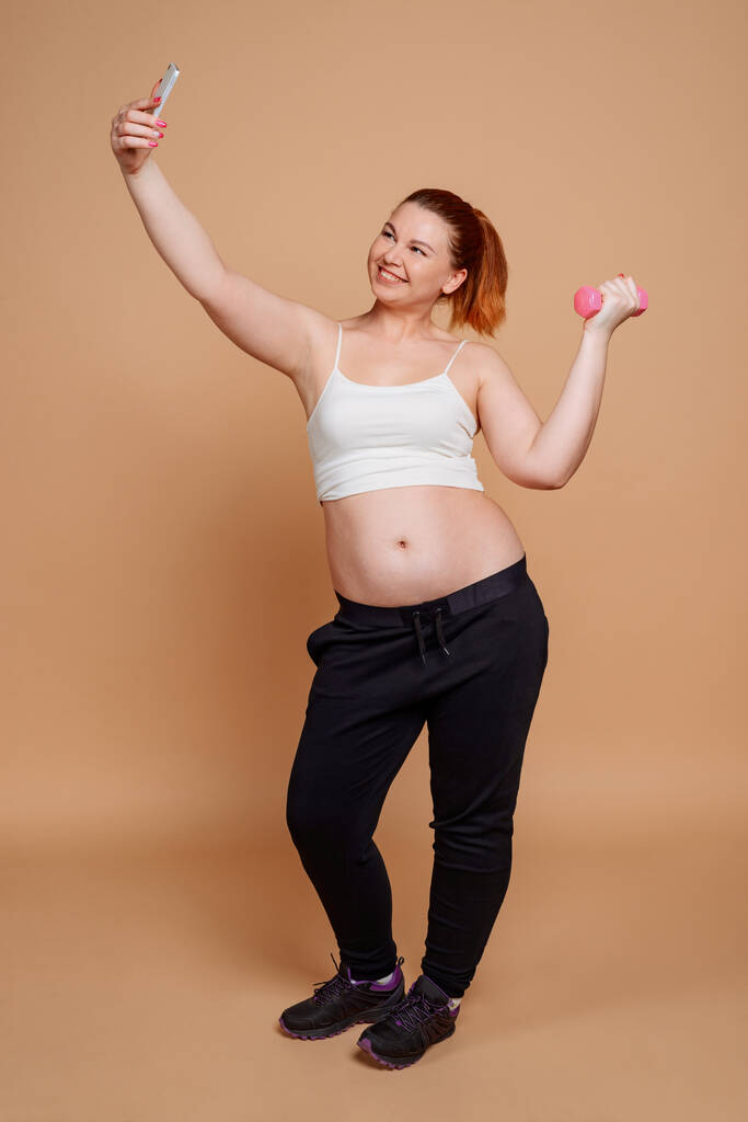 Mujer alegre tomando una selfie mientras hace un ejercicio de mancuerna
 - Foto, Imagen