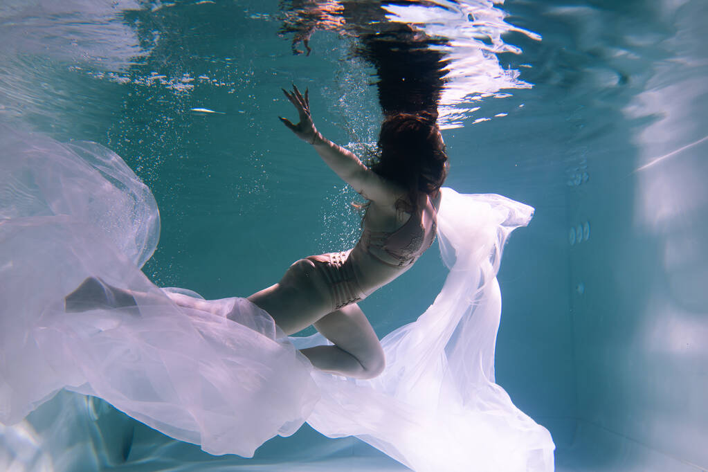 Belle gymnaste et sportive nage sous l'eau avec du tissu brillant dans la piscine - Photo, image