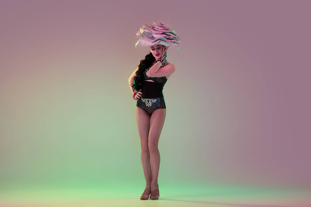 Young female dancer with huge floral hats in neon light on gradient background - Photo, Image