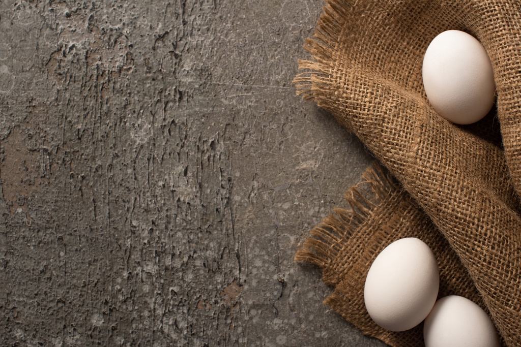 vista superior de huevos de pollo blancos sobre tela de saco sobre fondo texturizado gris
 - Foto, imagen