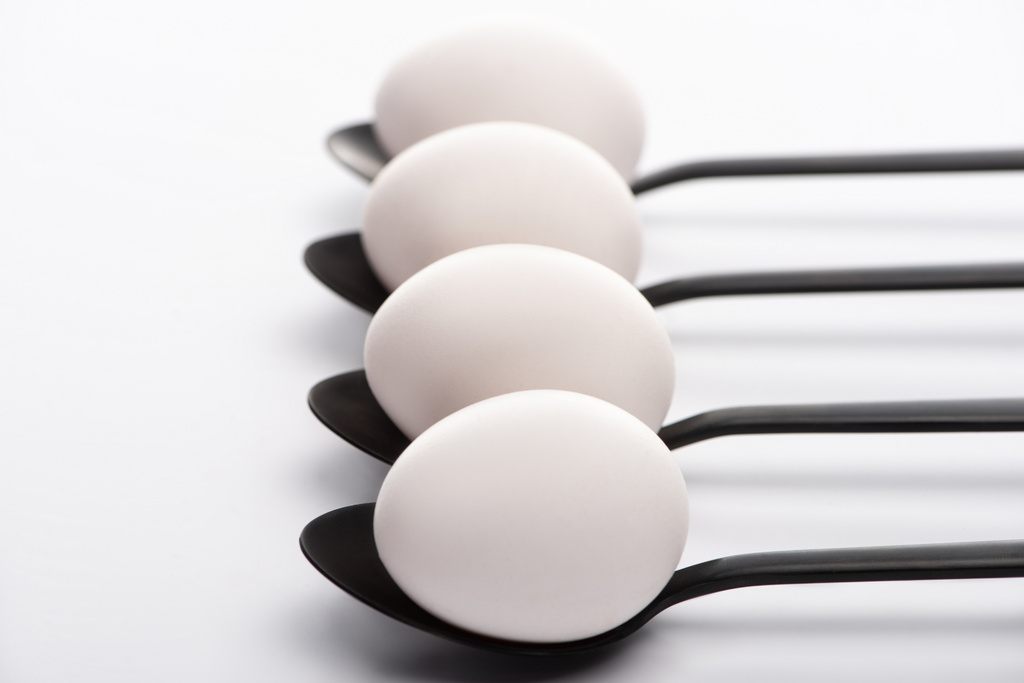 selective focus of white chicken eggs on black spoons on white background - Photo, Image